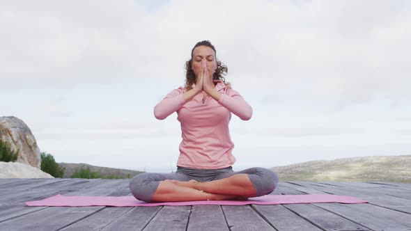 Caucasian woman practicing yoga meditation in lotus position on deck in rural mountainside setting