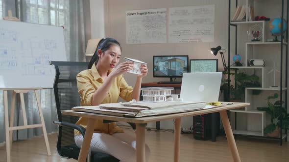 Asian Woman Engineer With A Laptop Making Paper Model Of House At The Office