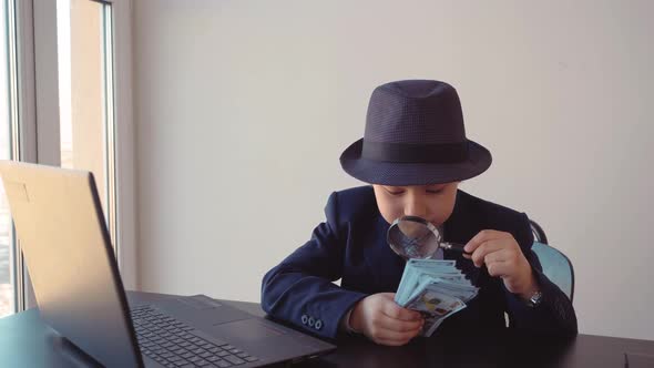 Child Boy Looks Like a Businessman in Hat and Suit is Checking Dollars with Magnifier