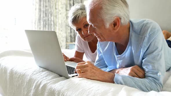 Smiling senior couple using laptop on bed in bedroom