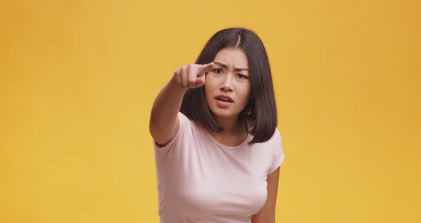 Angry Asian Woman Pointing Finger To Camera, Suspecting and Blaming in Lying, Orange Background