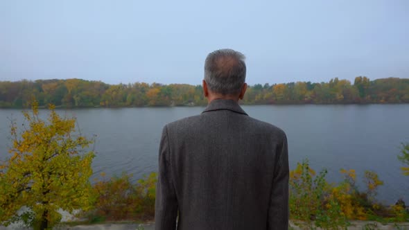 Aged Man on Bank of River in Fall