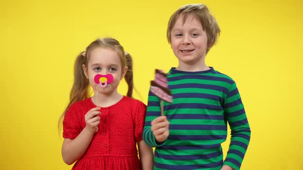 Cheerful Funny Little Girl with Baby's Dummy on Stick and Laughing Cute Boy with Printed Cake Posing