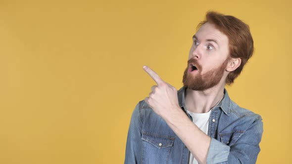 Redhead Man Pointing with Finger on Side Yellow Background
