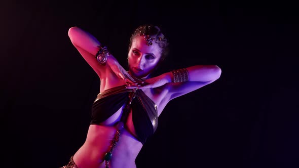 A Woman Dances an Oriental Belly Dance on a Dark Smoky Background in the Studio Making Beautiful