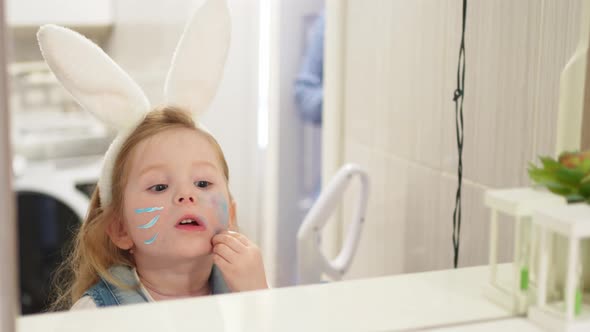 Little Girl Looks at a Mirror with a Painted Face and Tries to Wash