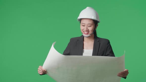 Asian Female Engineer With Safety Helmet Looking At Blueprint While Walking In The Green Screen