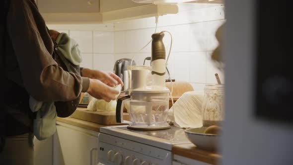 Mother carrying her baby on a sling uses food processor, medium shot pan left