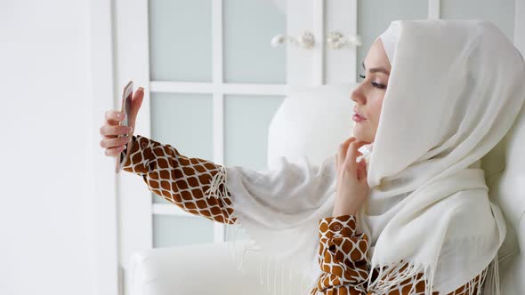 Young Muslim Woman in Hijab Is Making Selfie on Smartphone Sitting on the Sofa.