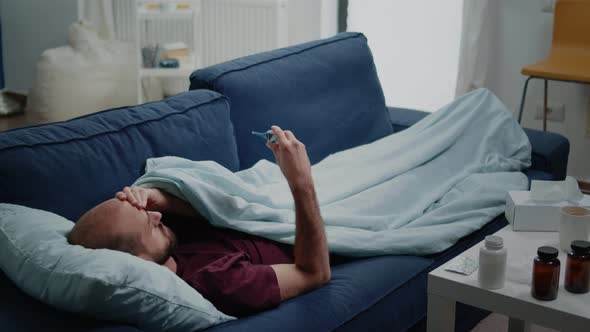 Man with Headache Holding Thermometer for Fever Measurement