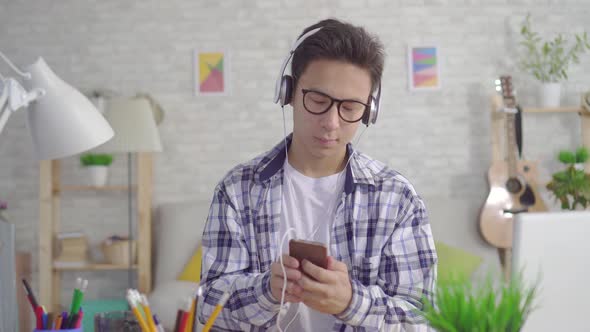 Young Asian Man with a Smartphone in Hand Listening To Music with Headphones