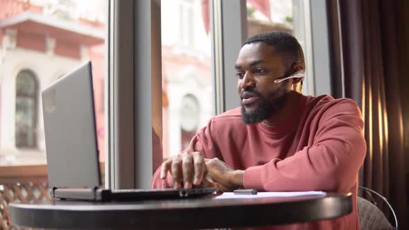 African American Young Man Wear Headset Communicating By Conference Call Speak Looking at Computer