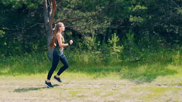 CU Young Girl Goes in for Sports in the Morning Runs Along a Pine Forest