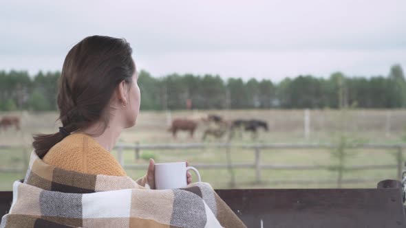 A girl covered with a blanket, drinks hot coffee from a white mug