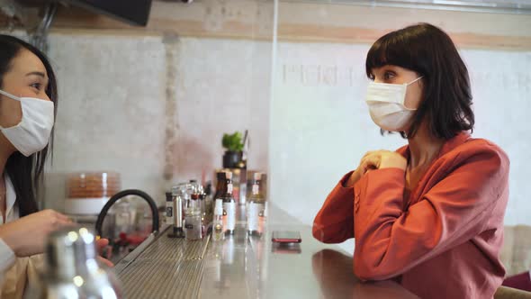 Woman customer receiving food from waitress with face mask on counter in restaurant during covid19.