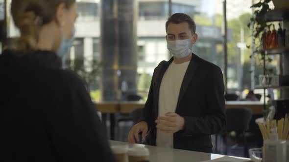 Positive Young Businessman in Covid-19 Face Mask Receiving Takeaway Coffee at Cafe Counter and