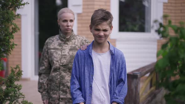 Zoom in to Desperate Teenage Boy with USA Flag Looking at Camera As Blurred Sad Military Mother