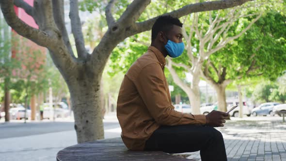 African american businessman wearing face mask using tablet sitting on bench