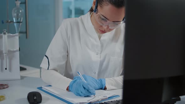 Woman Chemist Taking Notes and Using Computer for Experiment