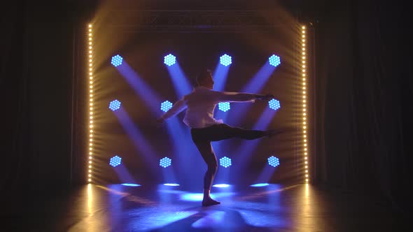 Professional Male Ballet Dancer Performs a Pirouette in a Dark Smoky Studio. Silhouette of Men