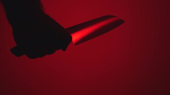 A man's hand holds a large kitchen knife against a red background