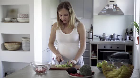 Smiling Future Mother Cutting Salad on Kitchen Table