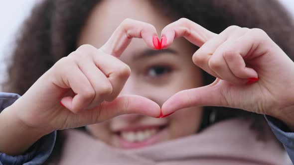 Head Shot Close Up Smiling Kind Afro Woman Showing Heart Symbol To Camera Makes Gesture of Love