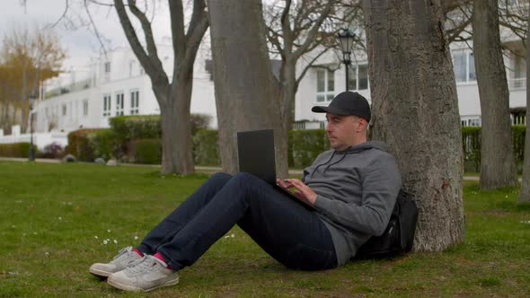 Young Man is Sitting in a Park in a Tourist Place Working on a Laptop