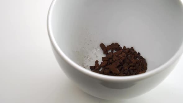 A serving of sublimated instant dried chicory root is poured from a teaspoon into an empty cup