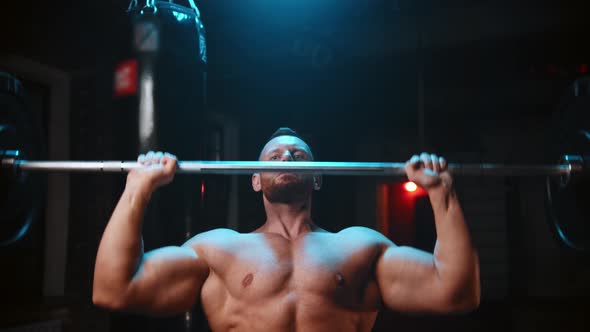 Tough Man Standing in the Gym and Lifts a Heavy Bar and Pumping His Hands Muscles Over His Head