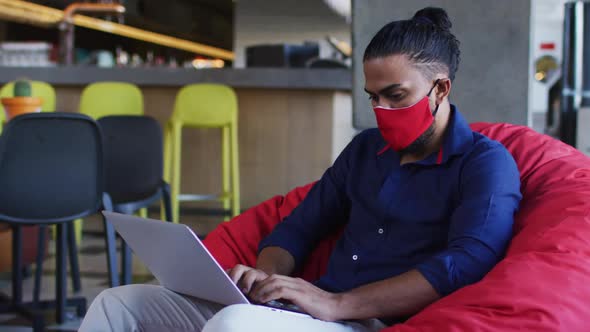 African american man wearing face mask sitting in cafe using laptop