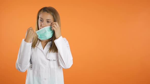 Young Beautiful Female Doctor Taking Off Surgical Face Mask and Breaths Deep and Slow