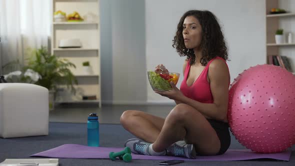 Mixed Race Woman Sitting on Floor in Sportswear and Eating Salad, Body Care