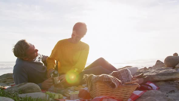 Caucasian couple enjoying free time by sea on sunny day eating and drinking coffee