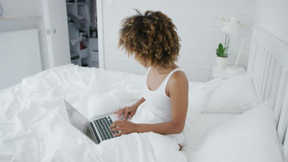 Pretty Woman Lounging on Bed with Laptop