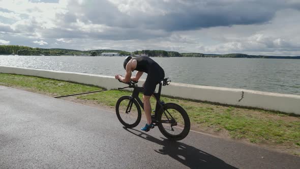 Triathlete Rides a Cutting Bike Pro Cyclist Rides on a Track Near a Lake Athlete Training for Race