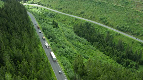 Aerial View of the Road with Driving Cars and Truck in the Mountains with High Green Fir Foliar Pine