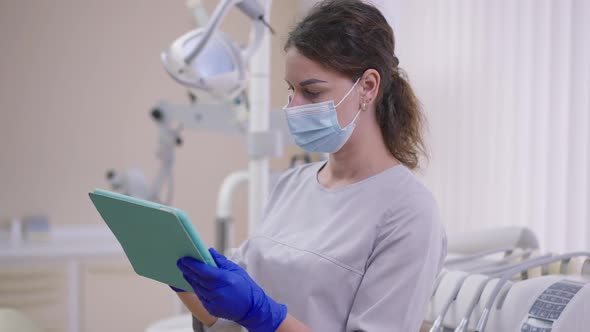 Professional Woman in Face Mask Examining Dental Xray on Tablet Standing in Office