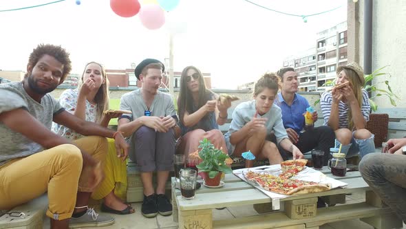 Young people sitting around the table and eating pizza on the rooftop terrace