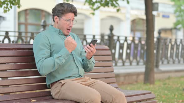 Man having Failure on Smartphone while Sitting on Bench