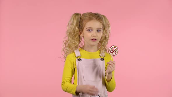 Beautiful Girl with a Lollipop in Studio on Pink Background