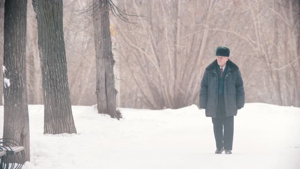 An Old Man Veteran Walking in the Snowy Park While Snowfall