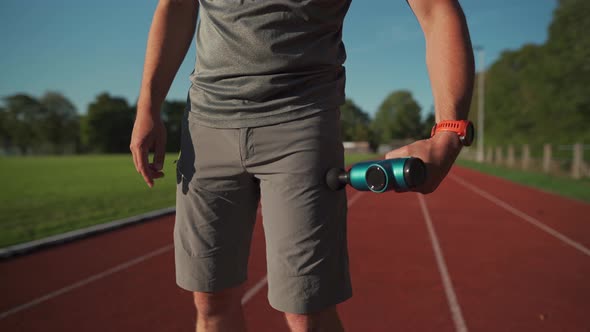 An Athlete Massages with a Percussion Therapy Gun to Relieve the Pain of Muscle Aches After a