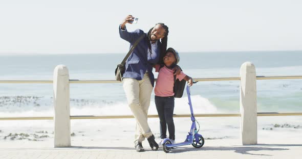 Video of happy african american father and son with scooter taking selfie on promenade