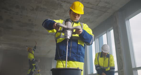 Professional Male Builder Mixing Plaster in Bucket Using Electric Mixer at New Renovating Apartment