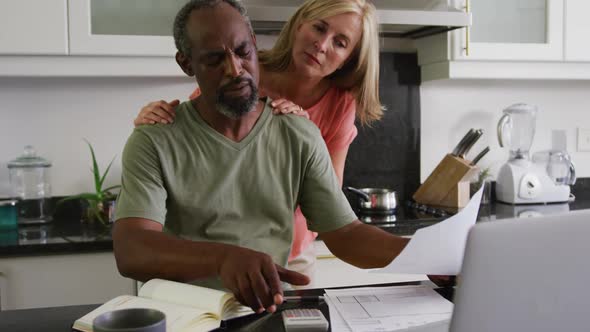 Concerned diverse senior couple using laptop computer paying bills in kitchen