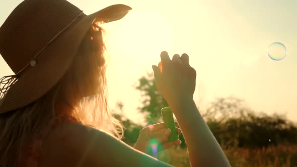 Happy Girl Blowing Soap Bubbles. Attractive Woman In Hat Relaxing On Morning Sun. Countryside Field.