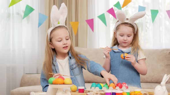 Little Girls with Rabbit Ears Celebrate Easter and Decorate Eggs with Paints