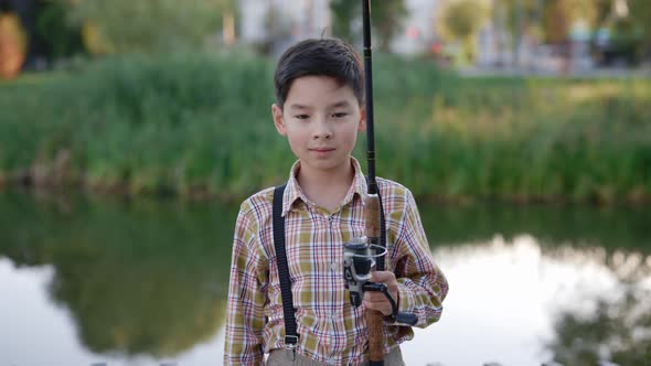 Portrait of the Young Smiled Boy Wearing Special Clothes for Fishing Holding the Fishing Rod