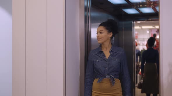 A Young African American Woman Exits an Elevator and Enters a Women's Clothing Store in a Mall